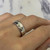 An image of a Chopard brand women's ring without stones, displayed on a finger, viewed at a slight angle showcasing the band's smooth, reflective surface. The ring is centered and occupies the middle portion of the frame, with a soft-focus background that provides a neutral setting emphasizing the ring's design. The photo is taken from a close distance, offering a clear view of the ring's details and craftsmanship.The ring is pre-owned and in great condition.