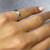An image of a Gucci icon GG ring without stones, worn on the ring finger of a woman's left hand. The hand is resting on a gray surface with the fingers slightly bent and angled towards the viewer, giving a clear view of the top and side of the ring. The ring appears to be white gold with engraved details, and it occupies the center of the image at a medium distance, allowing for a detailed view of the product.The ring is pre owned in a great condition. 