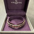 An image of a Charriol women's bracelet without stones, positioned in a circular shape at the center of an open, purple Charriol-branded box. The bracelet has a metallic finish with intricate, etched floral patterns and appears to be a medium distance from the camera, providing a clear view of its design and the texture of both the bracelet and the box's interior. The angle of the shot is from slightly above the box, allowing a full view of the bracelet and the brand logo on the box lid.