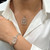 An image of a woman wearing a Rachel Koen necklace with diamonds and clear crystal gemstones. The necklace features a rectangular pendant with intricate detailing, positioned at the center of the chest. The angle is slightly above and close-up, capturing the elegance of the jewelry. The woman is wearing a white blouse, and part of a matching bracelet is visible on her wrist, complementing the necklace.Excellent pre-owned condition. 