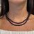 An image of a woman's necklace with gemstones, designed by Rachel Koen. The necklace features two strands of deep purple, round amethyst. It rests elegantly around the neck, viewed from the front at a close distance, with the shoulders and upper chest visible. The angle captures the necklace symmetrically, highlighting its layered design. Excellent pre-owned condition. 