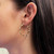 An image of a woman's ear wearing a gold twisted hoop earring without stones. The earring is positioned on the left ear, viewed from a side angle at close range, highlighting the earring's smooth and intricate design. The focus is on the earring, with the woman's dark hair framing the background.Excellent pre-owned condition. 
