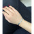 An image of a Hermes bracelet with diamonds, worn on a wrist. The bracelet is positioned horizontally across the wrist, viewed from above at a close distance. The angle captures the shiny metal and embedded diamonds, highlighting its sleek and elegant design. The background is a dark fabric, enhancing the bracelet's reflective qualities.