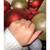 An image of a hand wearing a gemstone ring, positioned centrally and captured at a close angle. The ring, crafted in a yellow gold metal, features a design with small green emerald gemstones. The hand rests against a backdrop of large, glittery red and gold ornaments, enhancing the festive atmosphere.