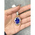 An image of a women's pendant by Rachel Koen featuring a large blue tanzanite gemstone at its center, surrounded by diamonds and ruby gemstones in yellow and white gold. The pendant is held in an open hand, viewed directly from above at a close distance. The background is a textured gray fabric. No chain included. Great preowned condition.