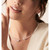 An image of a woman's neck wearing a Dinh Van necklace with diamonds. The necklace is elegantly positioned around the neck, featuring two prominent diamond accents at the both ends. The angle is slightly to the side, capturing the necklace from a close-up perspective, allowing for detailed visibility of the diamond settings and design.