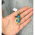 An image of a pendant without chain featuring a large, oval-shaped boulder opal gemstone with vivid blue and green hues, set in a yellow gold frame. The gold setting is intricately designed with a winding pattern adorned with small diamonds. The pendant is placed on an open palm, providing a close-up view that highlights its size and intricate details. The image is taken from a top-down angle, showcasing the pendant's design against a neutral fabric background. Excellent preowned condition.