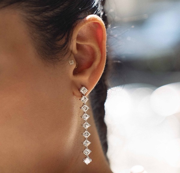 An image of baguette-cut yellow gold and white gold huggie earrings atop a grey fabric backdrop.