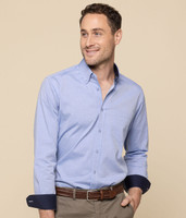 A button-up shirt in light blue with navy cuffs, featuring a chest pocket and a logo on the sleeve.