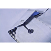 A close-up of a light blue button-up shirt, featuring a checkered inner collar and a dark button. The shirt has a logo.