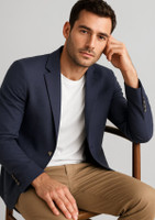 A navy blazer worn by a man, seated with a thoughtful expression, paired with a white T-shirt and tan trousers.
