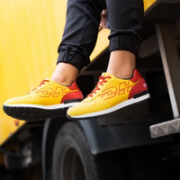 Person wearing yellow and red sneakers with geometric patterns, sitting on the edge of a vehicle with one leg crossed over the other.