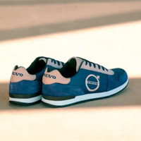 A pair of blue and beige athletic shoes with the Volvo logo on the side and heel, placed on a light-colored surface.