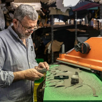 A craftsman meticulously works with leather pieces on a vibrant green table, surrounded by assorted materials and tools in a workshop.