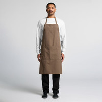 A man stands wearing a brown canvas apron over a white shirt, featuring a logo and front pockets.
