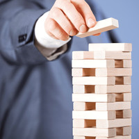 A hand placing a wooden block on a tall stack of light-coloured wooden blocks in a simple game setup.