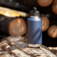 The Fridgy 1.9l All-Dayer in Navy Forge standing on a log. Wooden logs in the background. The sun is casting leavy shadows on the bottle and the logs.