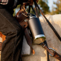 A Fridgy 1.9l All-Dayer in black is tied to a horse saddle. You can only see the jeans leg of the rider and parts of the palomino horses neck.