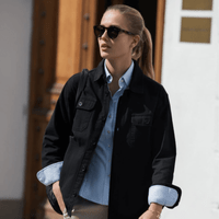 A unisex shirt in black, paired with a light blue shirt underneath, worn with sunglasses outdoors.