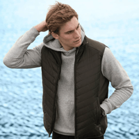 A green puffer vest worn over a grey hoodie, modelled by a young man against a water background.