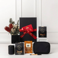 A black gift box tied with a red ribbon, containing coffee packets, a black mug, a pouch, and a pen.