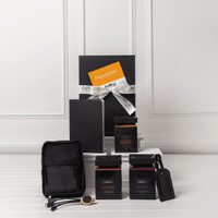 A travel kit featuring a notebook, two black boxes, a pouch, and a tag. All items are arranged on a white surface.