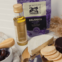 A gourmet gift pack with cheese, olives, olive oil, and biscuits, featuring a purple bag and wooden serving utensils.