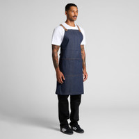 A denim apron with leather straps worn by a model, featuring a dark blue colour and a simple design.