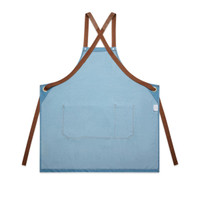 A denim apron in light blue with brown straps and a front pocket, featuring a small logo.