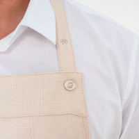 A light beige apron with a solid design and two front pockets. It features a branding logo on the strap.