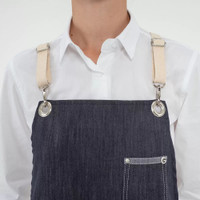A dark blue denim apron with beige straps, featuring multiple pockets and a logo.