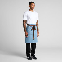 A denim half apron in blue with a brown tie, worn by a model in a white t-shirt and black pants.