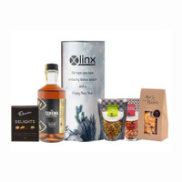 A whisky bottle, gourmet snacks, and chocolates arranged in a festive hamper with a cylindrical container.