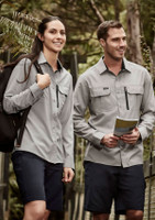 A women's long sleeve button-up shirt in light grey, worn with dark shorts, features a front pocket and branding.