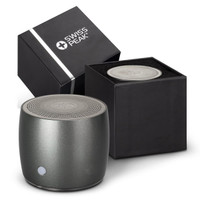 A round grey speaker with a textured top next to its black packaging, featuring a logo on the box.