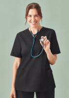 A woman in a black V-neck scrub top holds a stethoscope in front of a muted green background.