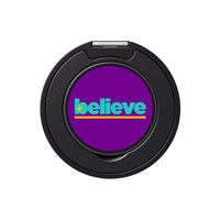A round phone grip and stand in black with a vibrant purple centre featuring the word "believe" in green and yellow.