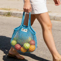 A blue mesh grocery bag filled with various colourful fruit is being carried by a person.