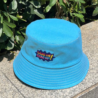 A bright blue bucket hat with an embroidered logo, resting on a stone surface surrounded by greenery.