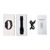 A slim black smart watch in a box, alongside a user manual and a USB charging cable.