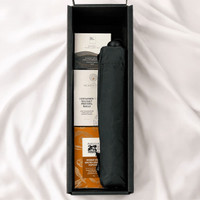 A black umbrella and snack items in a rectangular box on a soft surface.