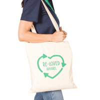 An organic cotton tote bag in cream with a green graphic design and logo on one side, held by a person.