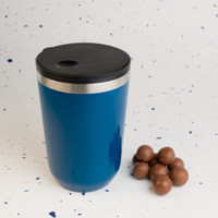 A reusable coffee cup in vibrant blue with a black lid, alongside a few chocolate-covered treats.