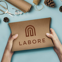 A person holding a brown, extra-large pillow box with a logo, surrounded by crafting materials and pinecones.