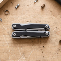 A silver and black multifunction tool displayed on a wooden surface, surrounded by small screws and metal fragments.