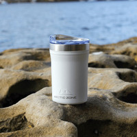 A drink bottle with a white exterior and a clear lid, featuring a branding logo, beside a rocky shore.