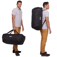 A duffel bag in black with a mid blue accent, featuring a shoulder strap and handles, held by a person.