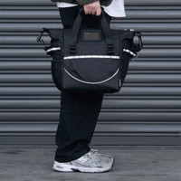 A cooler bag in black with strap and handles, featuring a logo, held by a person near a grey backdrop.