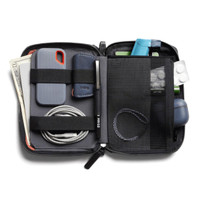 A compact, black toiletry bag containing a phone, cash, cables, a pen, and various small accessories. It features organisational straps.