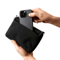 A black toiletry bag being held, with a smartphone and pen inside. The bag features a zip closure and a logo.